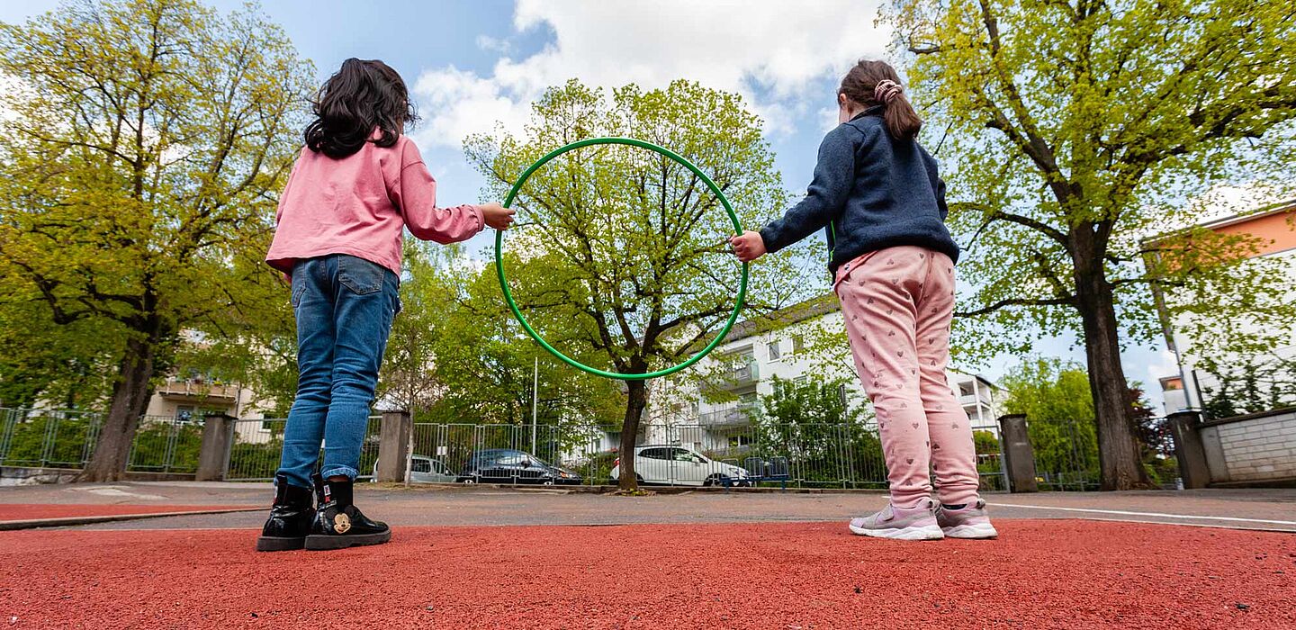 Zwei Kinder mit einem Hula-Hoop-ring, stehend auf dem Sportplatz der Helen-Keller-Schule
